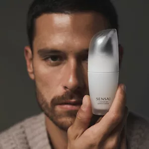 Close up of man holding Comforting Barrier Essence in hand next to their face